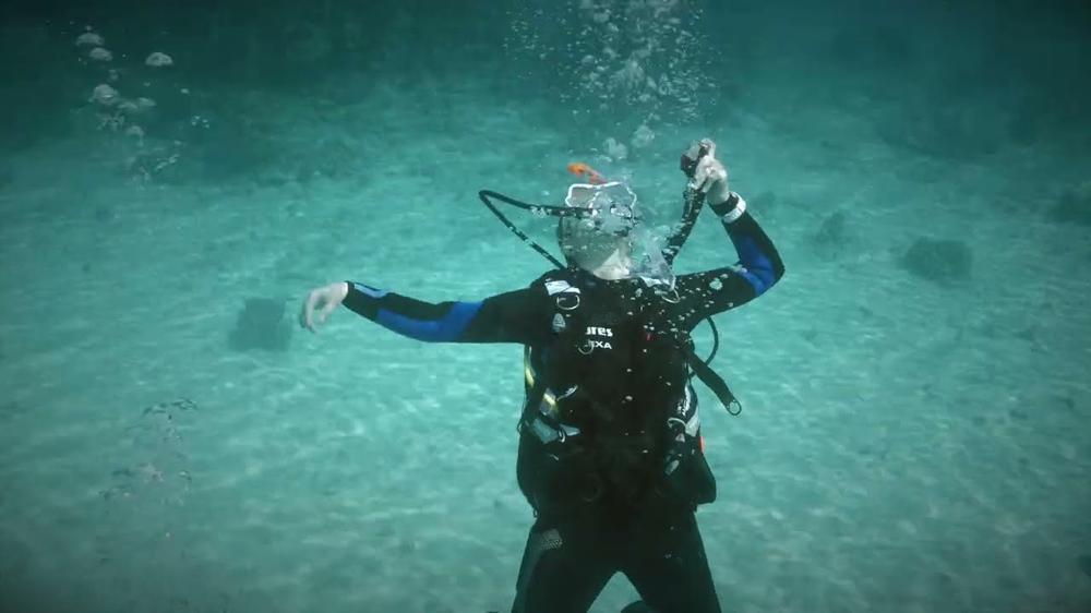 A scuba diver is swimming through a dark body of water.